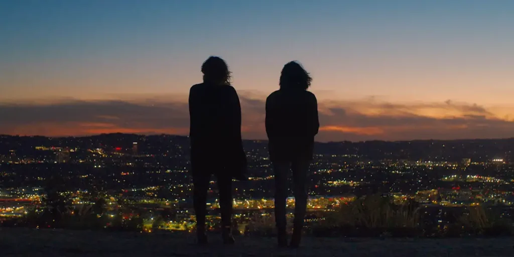 Two women look at a sunset from over the top of a hill in a still from the film American Meltdown