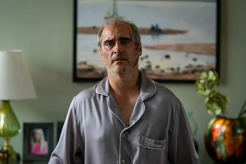 Joaquin Phoenix sits in a room looking puzzled with a picture behind him on the wall in a still from Beau is Afraid, a film that made us wonder about what makes confusing movies good