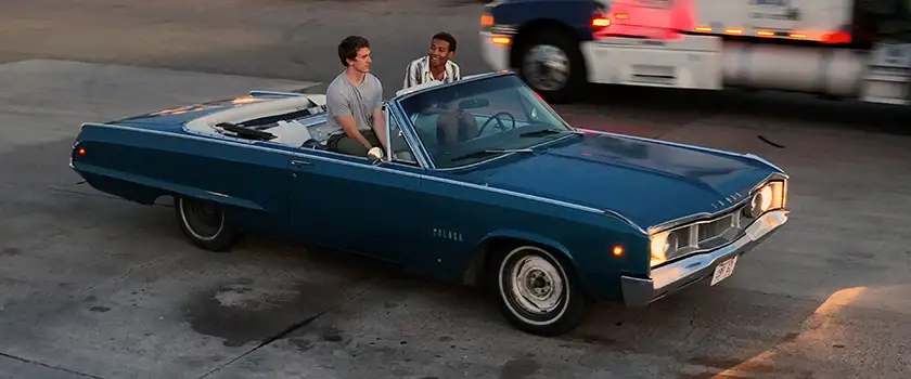 Two boys sit in a blue car in a still from the movie What We Find on the Road