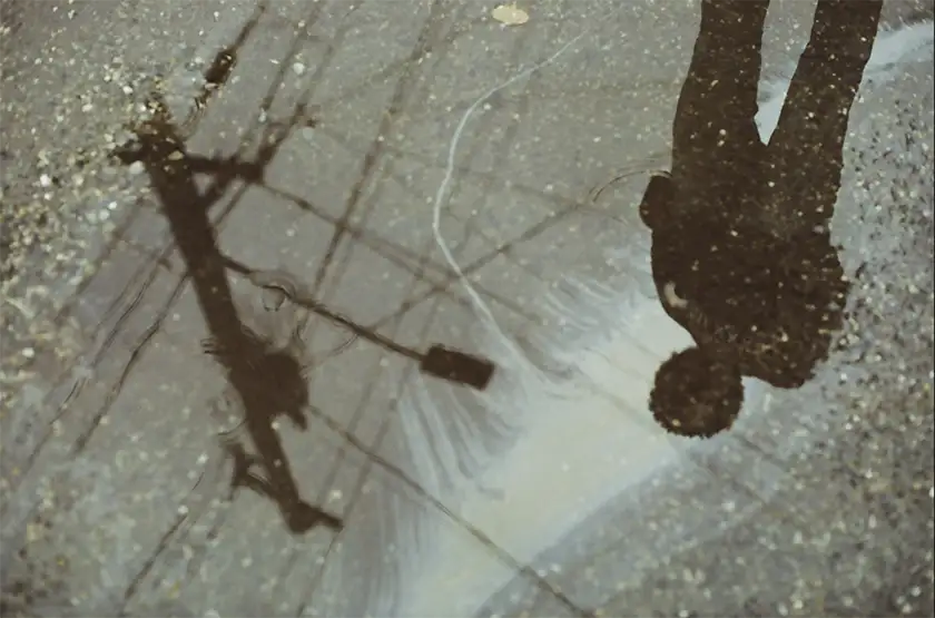 A boy and a traffic light's outline are  reflected in a puddle in a still from the film Know Your Place