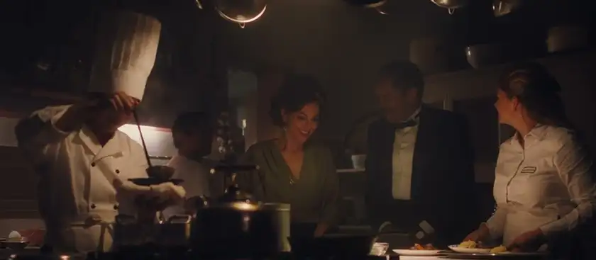 A chef is cooking at a restaurant's kitchen with some guests next to him in a still from the film Mistura