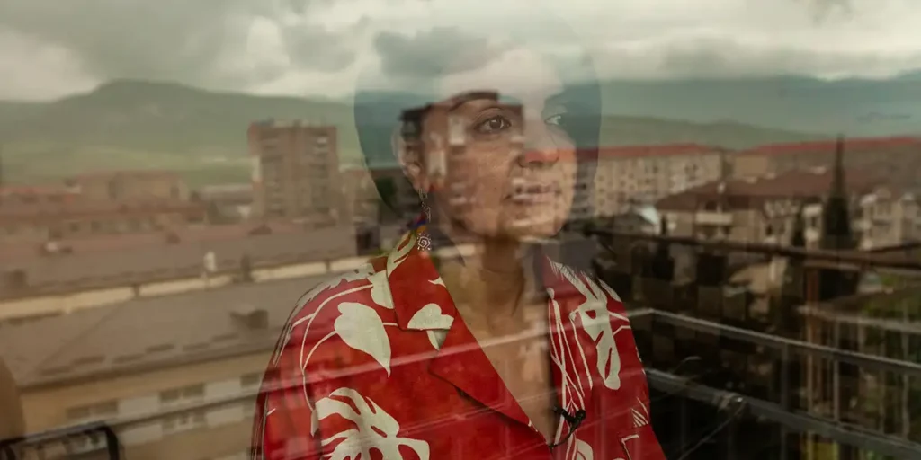 A woman with a red shirt looks out of the window in a still from the documentary film There Was, There Was Not