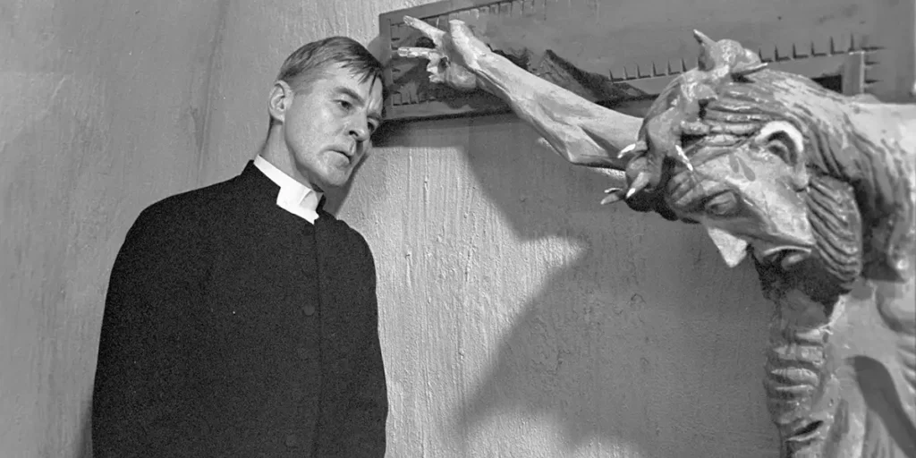 A priest looks at a crucifix that seems to be pointing at him in a still from the film Winter Light