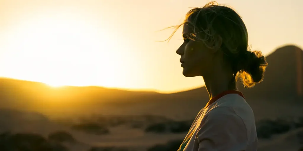 A blonde woman looks at the sunset in the desert in a still from the movie Catching Dust