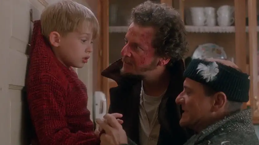 Two thieves look at a blonde boy (Macaulay Culkin) hanging off a door in Home Alone