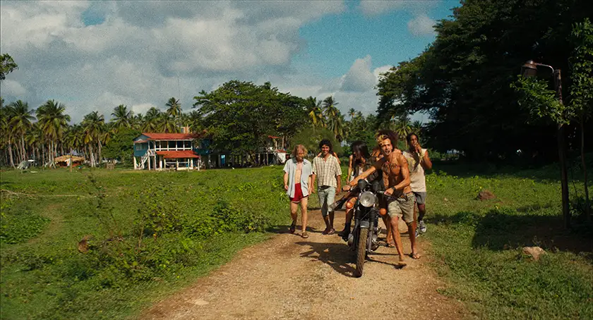 A group of people walk down a path with a motorbike in a still from the film Los Frikis