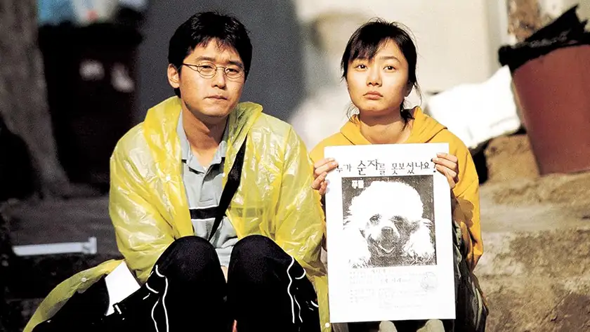 A girl holds the picture of a missing poodle sitting next to a boy, both looking sad, in Barking Dogs Never Bite, one of all the Bong Joon-ho movies ranked from worst to best in this list