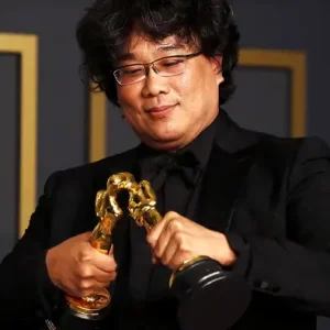 Director Bong Joon-ho holds two Oscars as if they were kissing