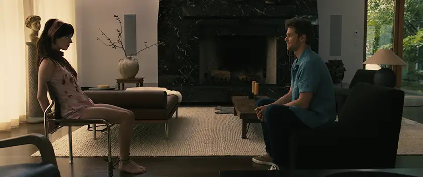 Sophie Thatcher as Iris is tied to a chiar and Jack Quaid as Josh is sitting opposite her, on an armchair, looking at her, in the movie “Companion”