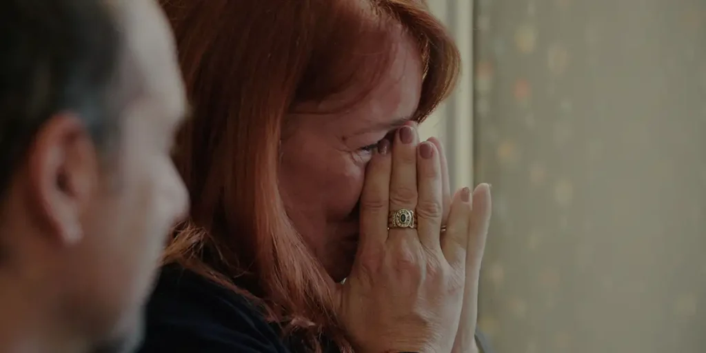 A woman's crying face as she touches her eyes with her fingers, her hands in prayer, in a still from GEN_ by Gianluca Matarrese