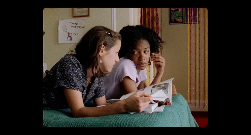 Two girls lean on a bed reading a diary together in a still from the film Girls Town