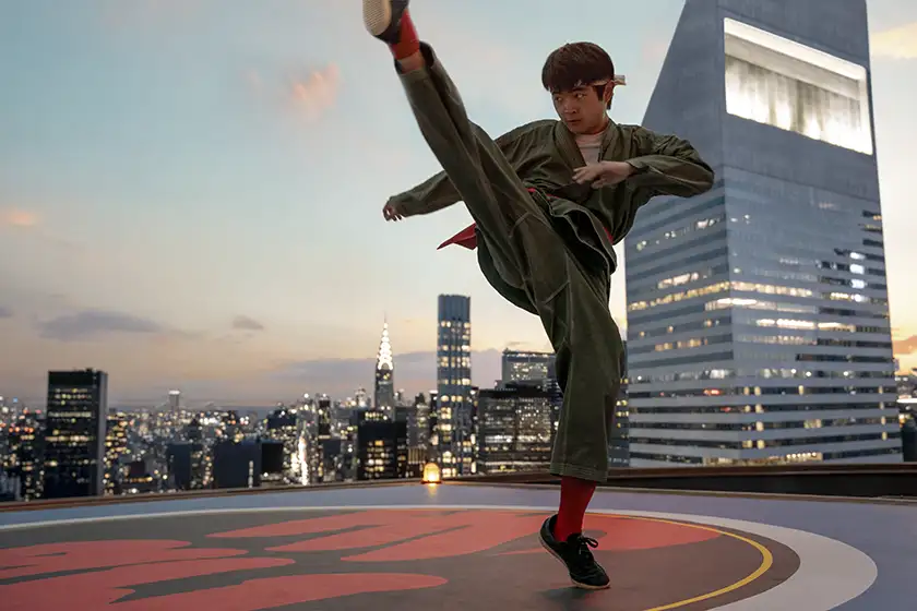 Ben Wang does a martial arts move on a rooftop with a leg raised up in the air in a still from Karate Kid: Legends, featured in an article with everything we know about the movie