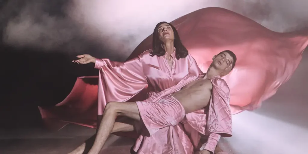 A mother holds his unconscious son looking at the sky in a pose that resembles religious imagery, with both wearing pink, in a still from the Eduardo Casanova film La Pietà