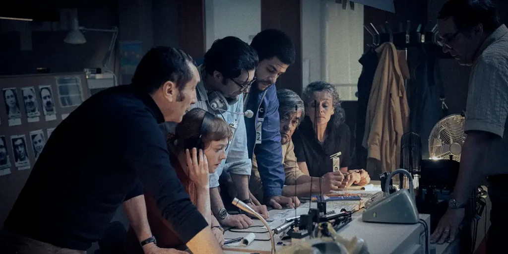 Jacques Lesgardes (Zinedine Soualem),Marianne Gebhard (Leonie Benesch),Geoff Mason (John Magaro),Carter (Marcus Rutherford) stand together leaning on a desk at a radio station in the film September 5