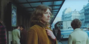 A woman wears a yellow coat at a station and looks sad in Les Rendez-vous d'Anna