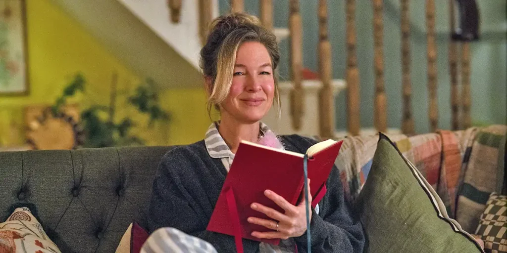 Renée Zellweger as Bridget Jones holds a red book while sitting on a sofa in Bridget Jones: Mad About the Boy