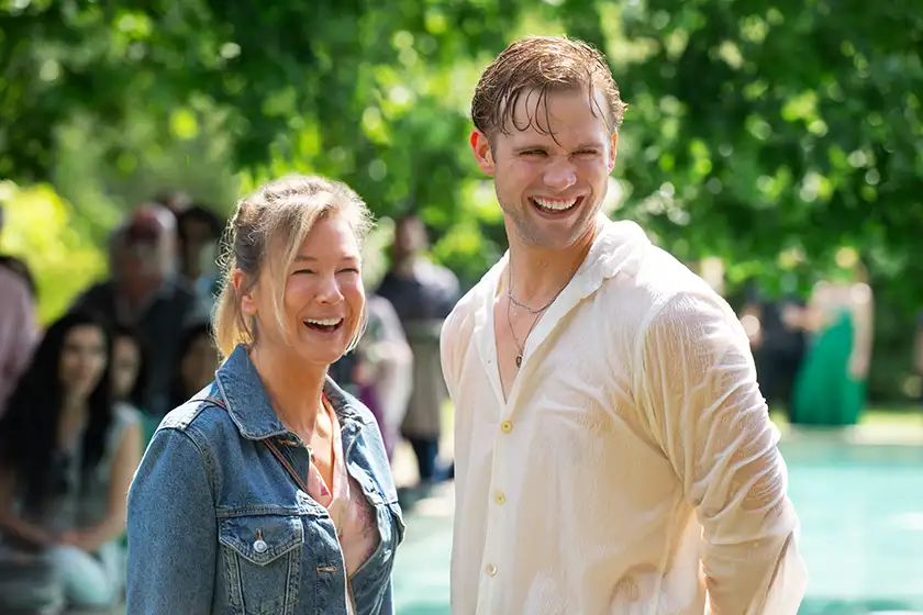 Bridget Jones (Renée Zellweger) smiles wearing a jeans jacket and Roxster (Leo Woodall) smiles too, with a wet white t-shirt, in Bridget Jones: Mad About the Boy