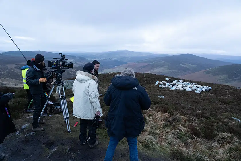 Actor Christopher Abbott, Director Christopher Andrews, whom we interview, and the crew standing on the set of Bring Them Down, filming sheep on a hill