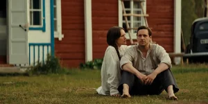 A man and a woman sit on the grass in front of a house in a still from the movie Raptures (Rörelser)