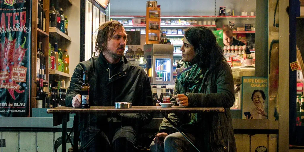 A man and a woman sit by a wooden table in a still from The Light (Das Licht)