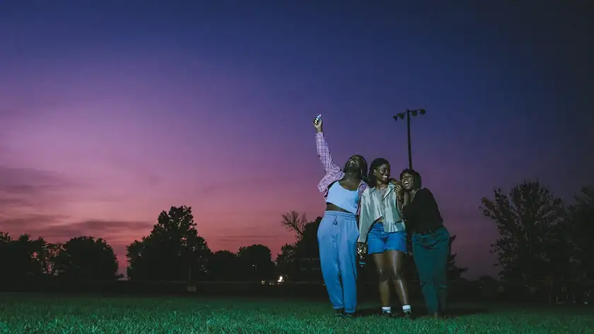 Three girls take a selfie outdoors at sunset in a still from the film Dreams In Nightmares, one of the 10 Movies to Watch at BFI Flare 2025 according to Loud And Clear Reviews