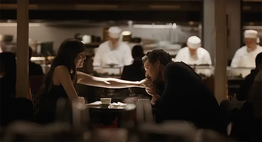 Pedro Pascal kisses Dakota Johnson's hand at a restaurant in a still from Celine Song's movie Materialists, which this article tell us everything we know about