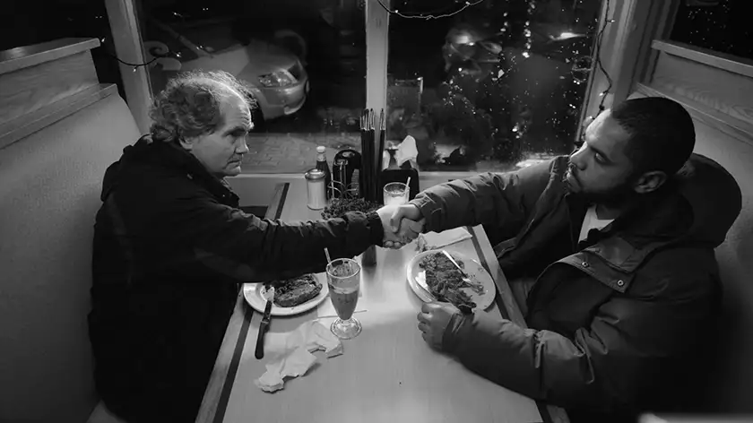 Erik Bjarnar and Darryle Johnson shake hands at a diner in a black and white still from the movie Stationed at Home