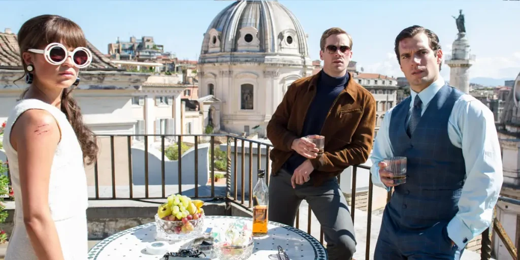 A woman and two men stand on a rooftop by a table with some breakfast on it in the movie The Man from U.N.C.L.E.