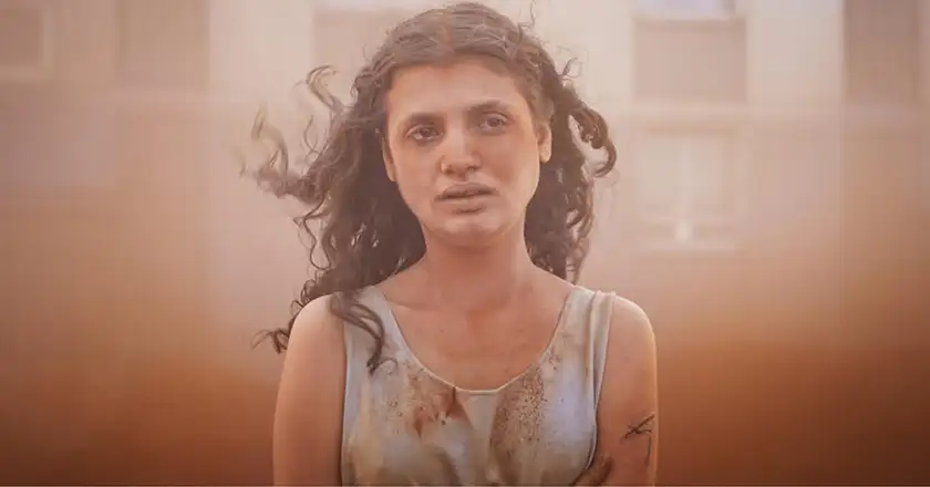 A woman stands in the dust in a still from the film Alpha, one of the 20 movies to watch at the 2025 Cannes film festival according to Loud and Clear Reviews
