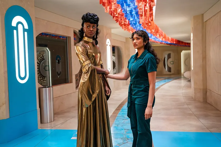 Two young women hold hands in a hallway in a still from Season 15 (also known as Season 2) Episode 6 of Doctor Who (2025), titled "The Interstellar Song Contest"