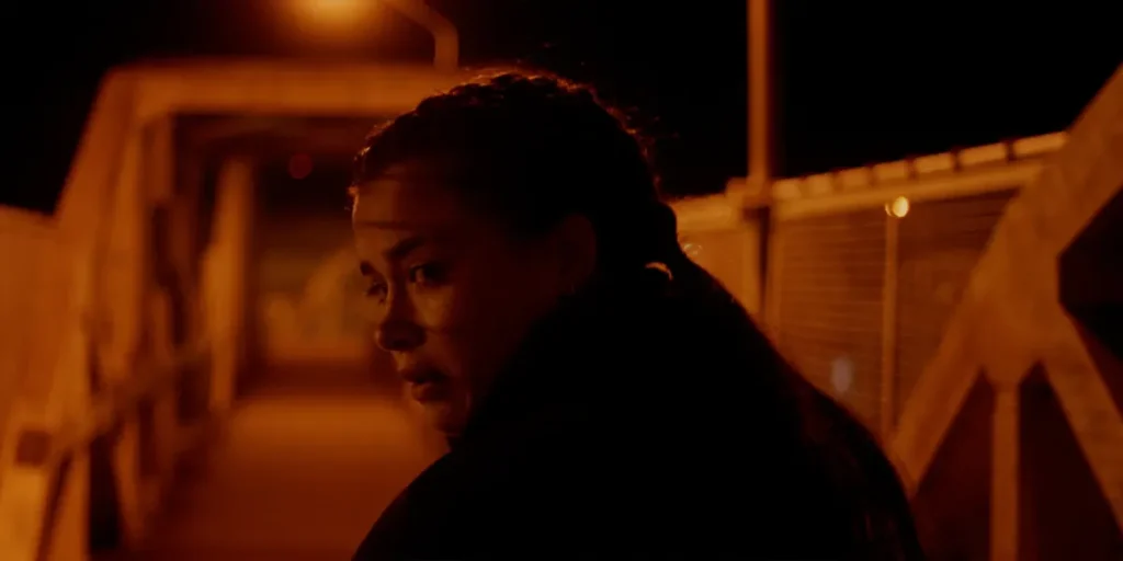 A young woman looks behind her before crossing a bridge at night in a still from the film Entroncamento (Night Passengers)