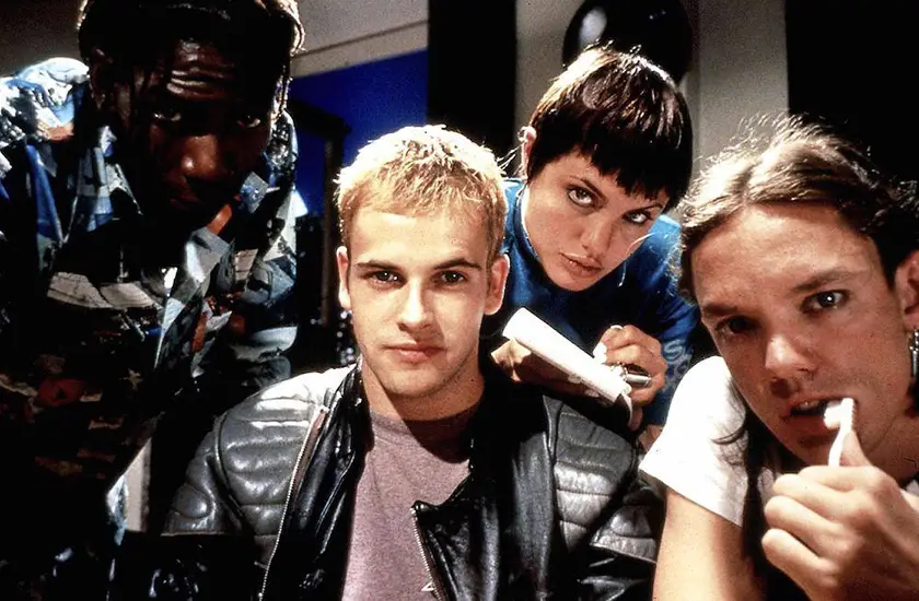 A group of teenagers look at a computer in a still from Hackers seen from the point of view of the computer screen
