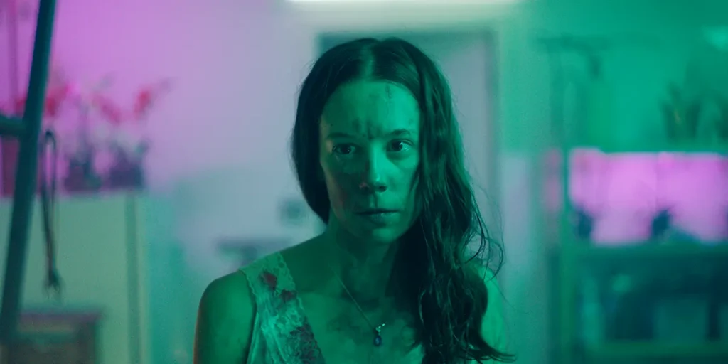 A young woman looks distressed in a green and pink-tinged still from the movie Kryptic