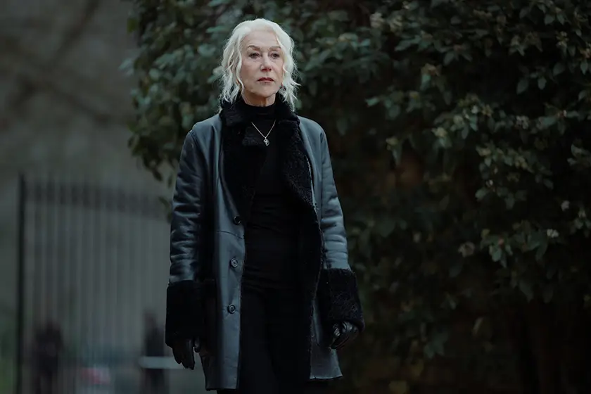 Helen Mirren stands outdoors, wearing a grey coat, as Maeve Harrigan in MobLand Season 1 Episode 9