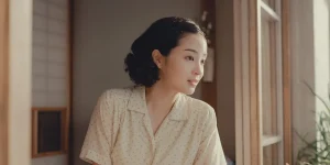 A woman looks outside the window in a still from A Pale View of Hills