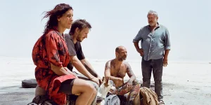 A woman and three men sit at the desert in a still from the film Sirât