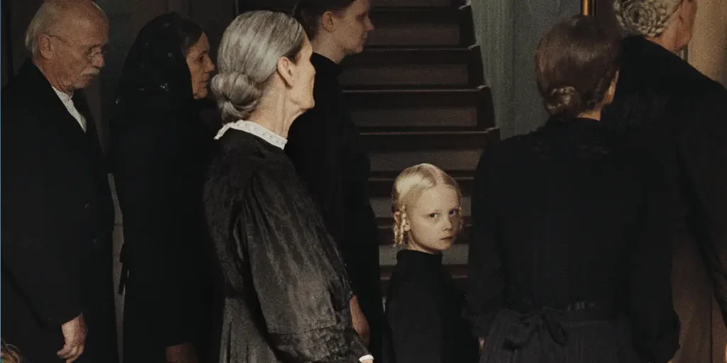 A child dressed in black stares at the camera surrounded by other people dressed in black, looking elsewhere, in a still from the movie Sound of Falling