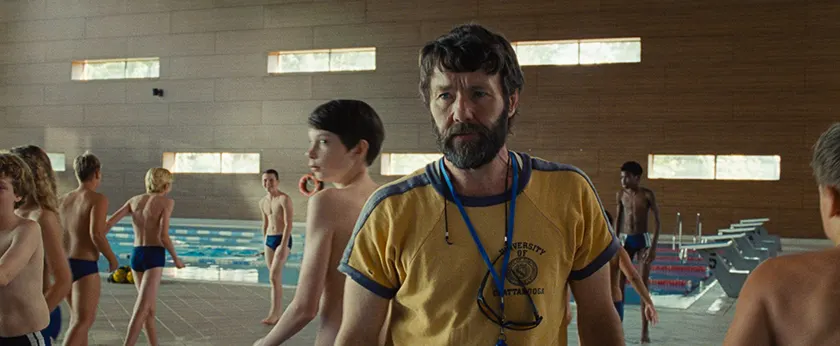 Joel Edgerton wears a yellow t-shirt by the swimming pool in a still from Charlie Polinger's 2025 film The Plague