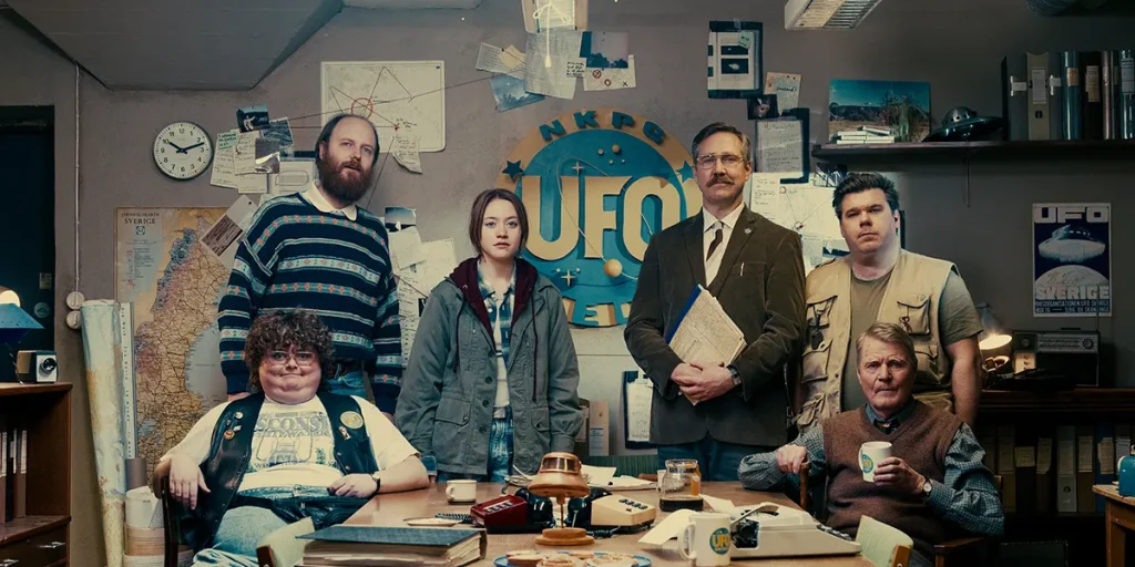 A team of UFO researchers pose for a picture in a still from the movie Watch the Skies