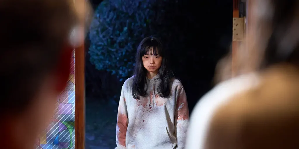 Kotone Furukawa wears a bloody jumper in a hallway in a still from the horror movie Best Wishes to All (2025)
