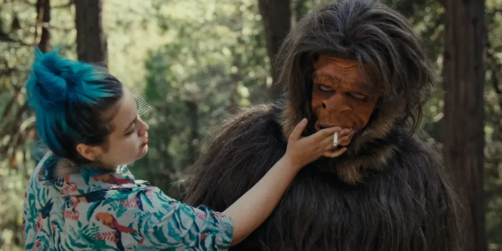 A woman helps a person in a Bigfoot costume smoke a cigarette in the movie Found Footage: The Making Of The Patterson Project