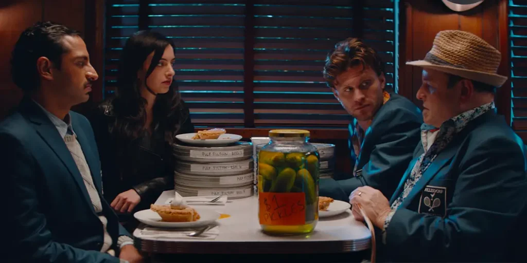 Three men and a woman sit across each other at a table in a scene from Stealing Pulp Fiction