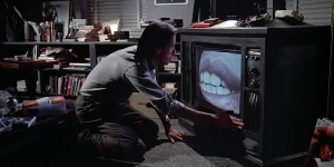 A man touches a TV screen showing a close-up of a woman's mouth in Videodrome, which predicts our addictions