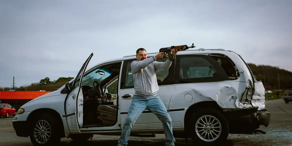 Nick Offerman stands by a car pointing a gun at someone in the 2025 movie Sovereign