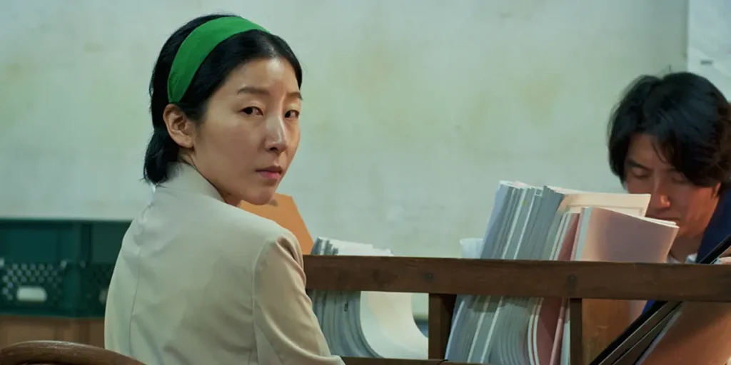 A woman sits and turns around to look into the camera in a still from the film The Woman (더 우먼)