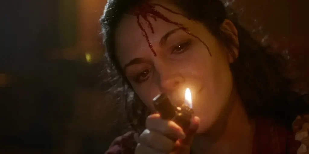 A woman with a bloody cut on her forehead lights up a cigarette in a still from the horror movie Lilly Lives Alone