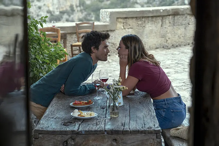 KJ Apa and Madelyn Cline lean into each other from across a table in The Map That Leads to You