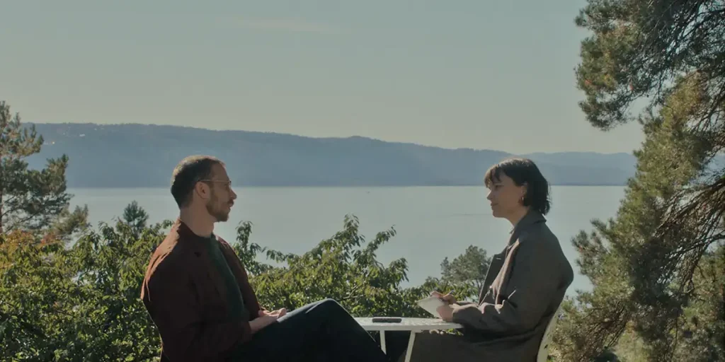 Herbert Nordrum and Lisa Loven Kongsli sit across each other at the lake in a still from Solomamma