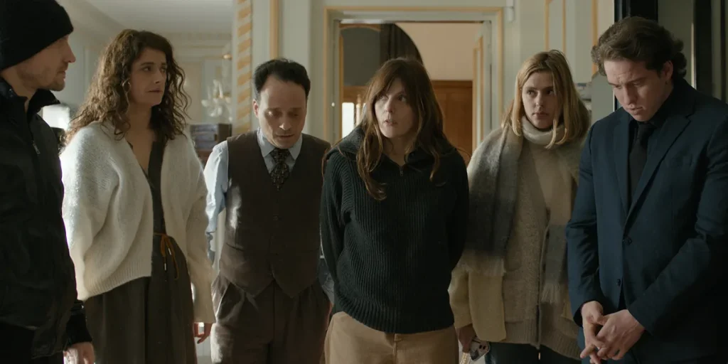 Valérie Donzelli, Frédéric Pierrot, Marie Vialle, Valentin Pradier, Emma Ravier, Mathieu Spinosi, and Daniel Garlitsky stand in a circle looking at each other in the film The Musicians (Les Musiciens)