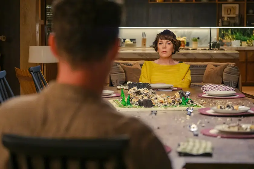 Olivia Colman stares at Benedict Cumberbatch from across the table looking upset in a still from the movie THE ROSES (2025)
